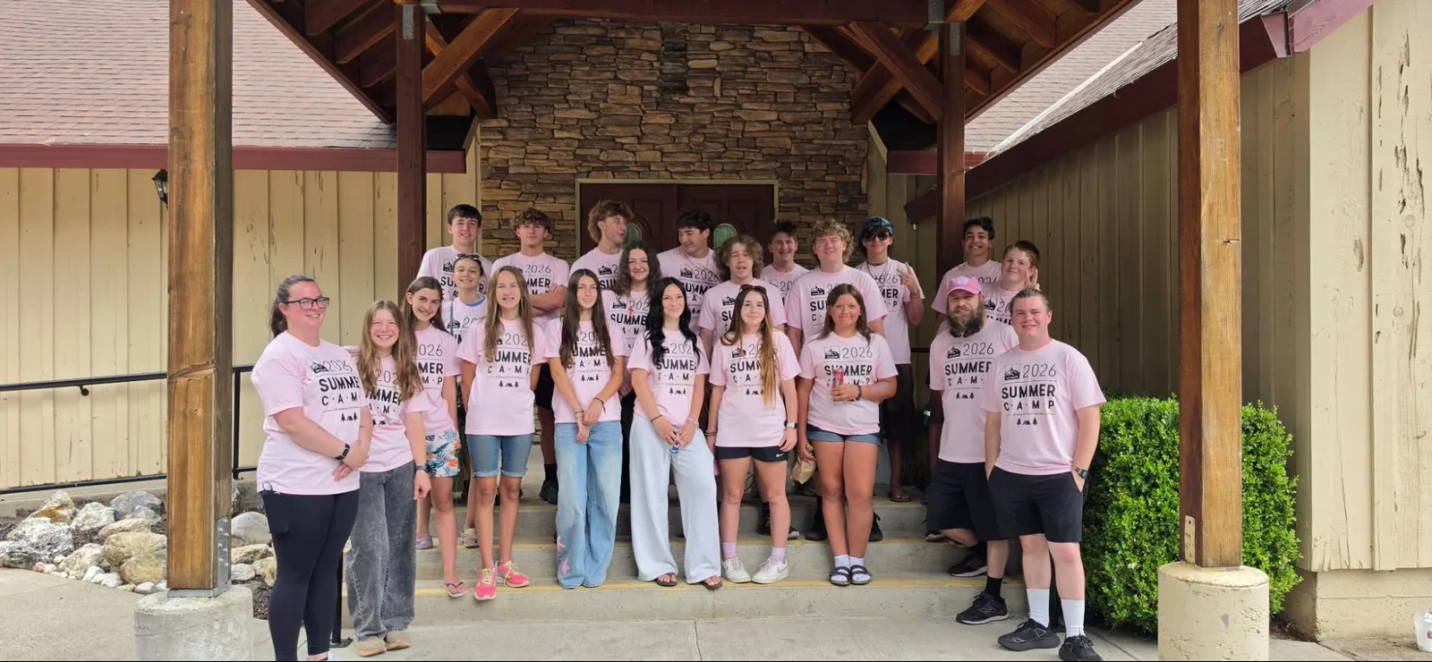 Youth group in matching pink camp shirts outside a lodge
